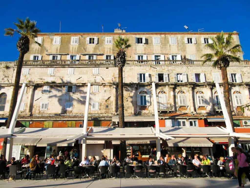 Looking at a group of restaurants on the Riva in Split with outdoor seating and umbrellas. Split vs Dubrovnik, Croatia