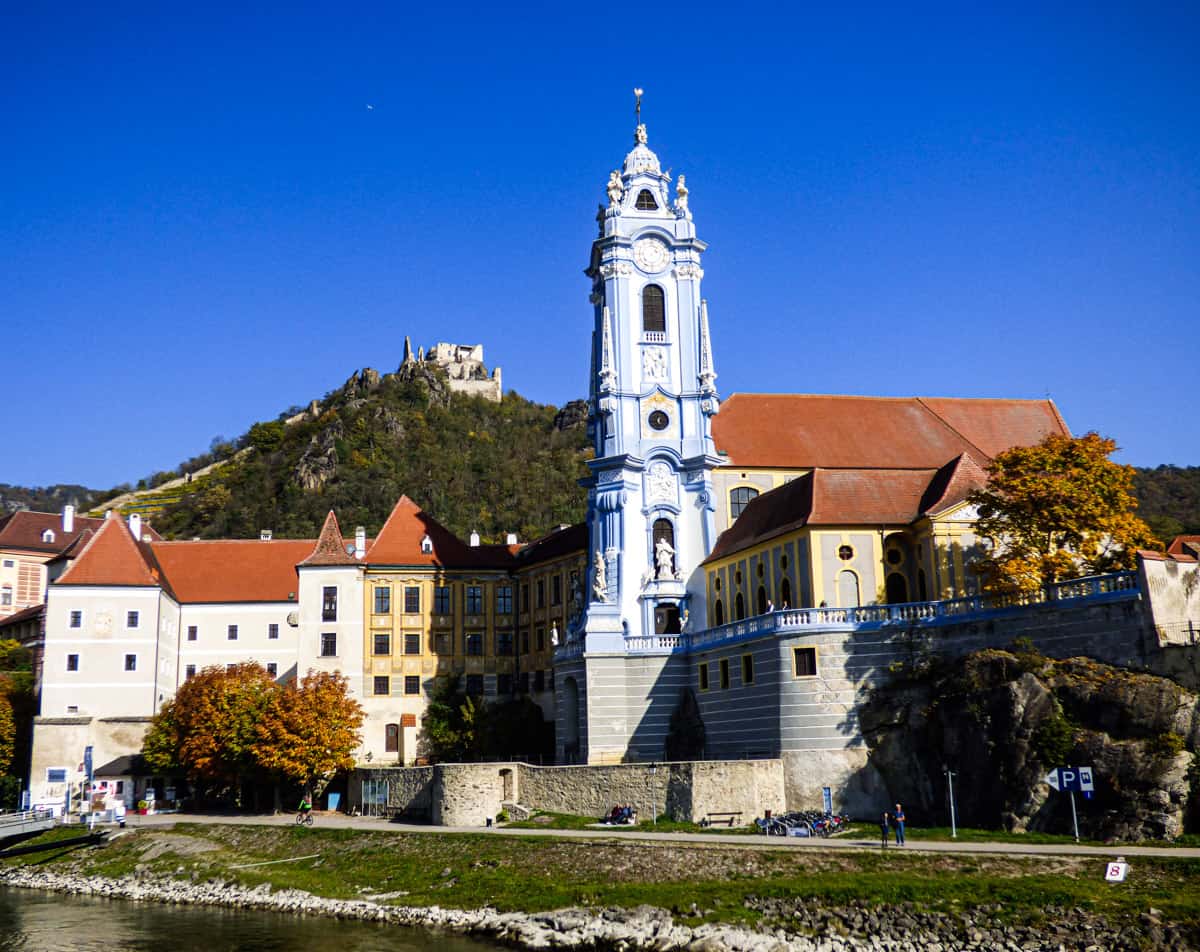 Light blue church tower surrounded by red roofed buildings and a castle on a hill in the background