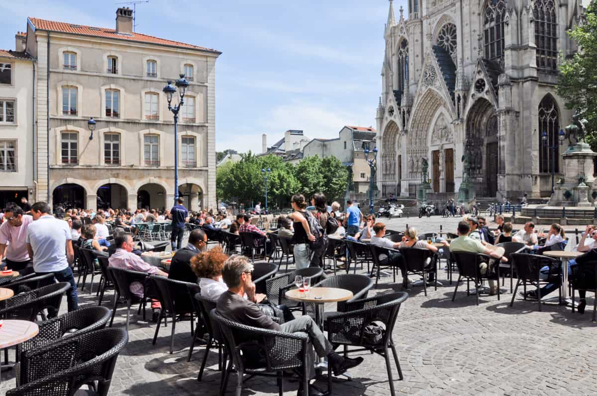 People siting at tables in a square in front of a cathedral in Nancy France