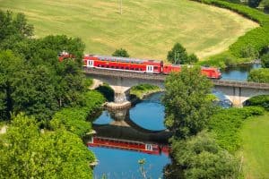 Red train crossing a bridge in the countryside is the cheapest way to travel Europe