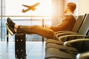 man sitting at airport with feet up on luggage